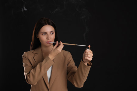 Woman using long cigarette holder for smoking on black background, space for textの写真素材