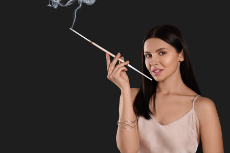 Woman using long cigarette holder for smoking on black background, space for textの写真素材