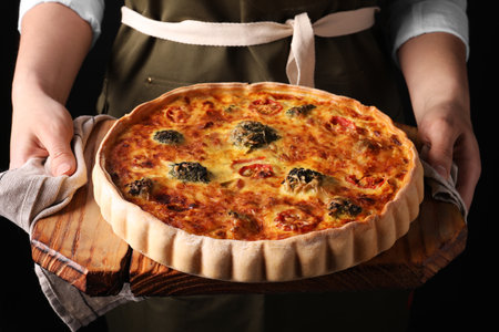 Woman holding delicious homemade vegetable quiche on black background, closeupの写真素材