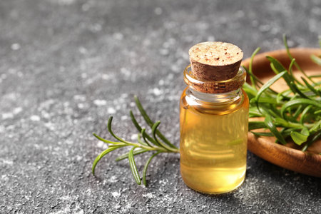 Bottle with essential oil and fresh rosemary on gray textured table, closeup. Space for textの写真素材