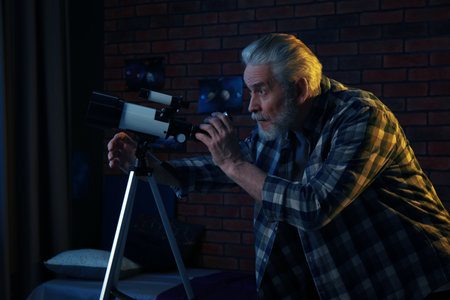 Senior man looking at stars through telescope in roomの写真素材