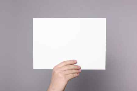 Woman holding sheet of paper on gray background, closeup. Mockup for designの写真素材