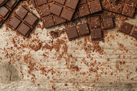 Pieces and shavings of tasty chocolate bars on wooden table, flat lay. Space for text