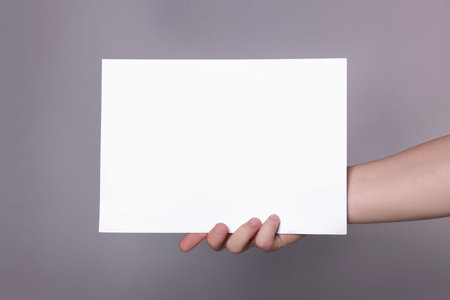 Woman holding sheet of paper on gray background, closeup. Mockup for designの写真素材