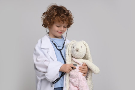 Little boy playing doctor with toy bunny on light grey backgroundの写真素材