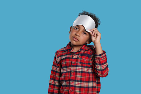 Boy with sleep mask on light blue background. Insomnia problemの写真素材
