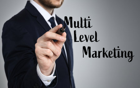 Man writing text Multi Level Marketing with marker on glass board against grey background, closeupの写真素材