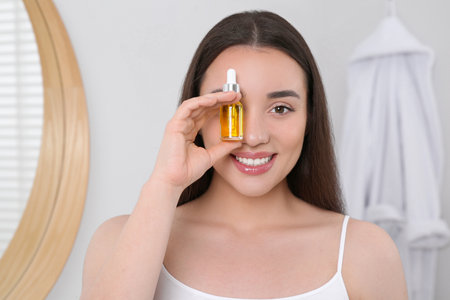 Happy young woman with bottle of essential oil in bathroomの写真素材