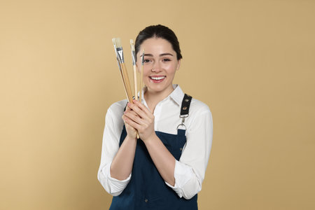 Woman with paintbrushes on beige background. Young artistの写真素材