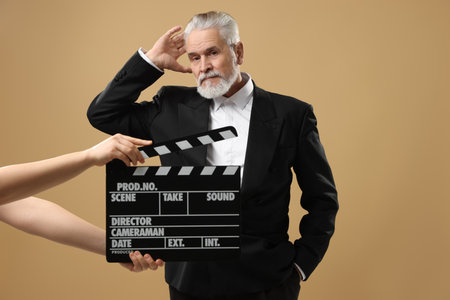 Senior actor performing role while second assistant camera holding clapperboard on beige background. Film industryの写真素材