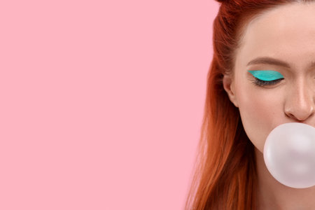 Beautiful woman with bright makeup blowing bubble gum on pink background, closeup. Space for textの写真素材