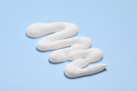 Sample of shaving foam on light blue background, closeup