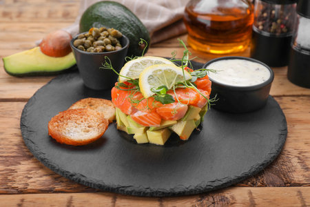 Delicious salmon tartare served with avocado, sauce and croutons on wooden table, closeupの写真素材