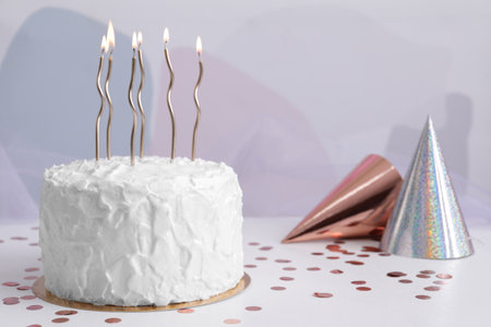Delicious cake with burning candles and party hats on white table. Space for textの写真素材