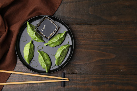 Delicious green dumplings (gyozas) with soy sauce served on wooden table, flat lay. Space for textの写真素材