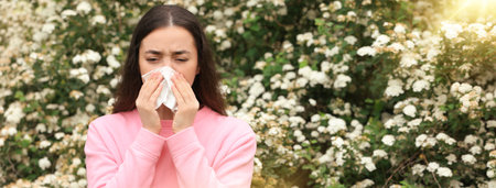 Woman suffering from seasonal pollen allergy near blossoming tree on spring day. Banner design with space for textの写真素材