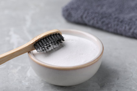 Bamboo toothbrush and bowl of baking soda on light gray table, closeup