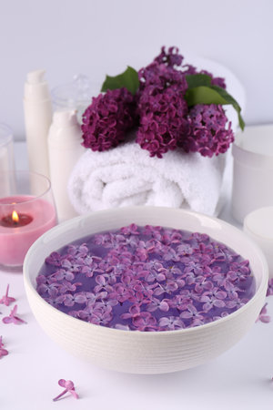 Bowl of water with lilac flowers, spa products and burning candle on white tableの写真素材