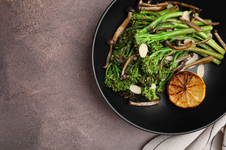 Tasty cooked broccolini with lemon and mushrooms on gray table, top view. Space for textの写真素材