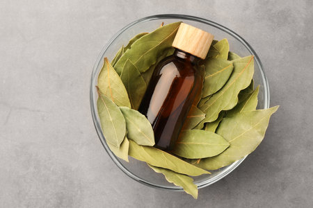 Bottle of bay essential oil and fresh leaves in bowl on light gray table, top viewの写真素材