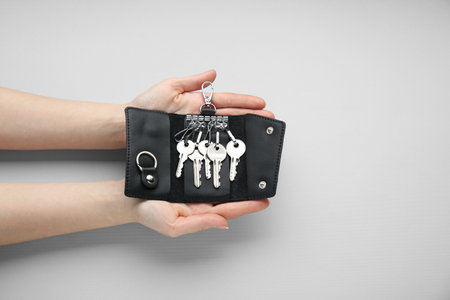 Woman holding open leather holder with keys on light gray background, top view