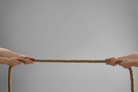 Dispute concept. Men pulling rope on light gray background, closeup. Space for textの写真素材