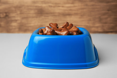 Blue bowl with bone shaped dog cookies on light table, closeupの写真素材