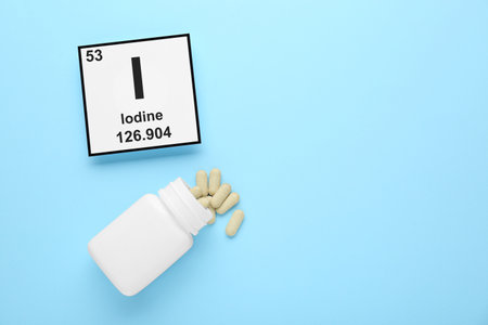 Plastic jar and iodine pills on light blue background, flat lay. Space for textの写真素材