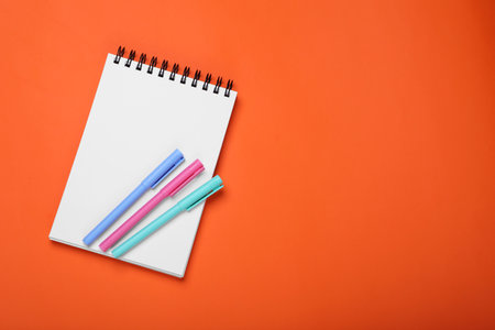 Blank office notebook and pens on orange background, top view. Space for text