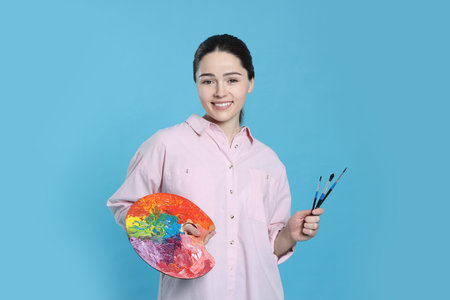 Woman with painting tools on light blue background. Young artistの写真素材