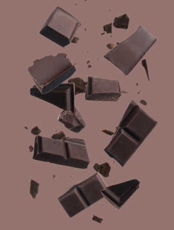 Pieces of chocolate bar falling on pale brown background