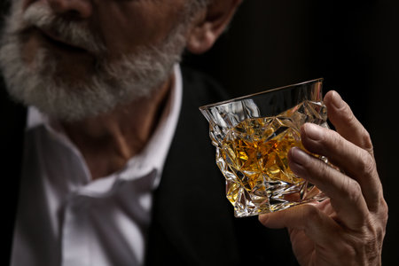 Man holding glass of whiskey with ice cubes on dark background, closeupの写真素材