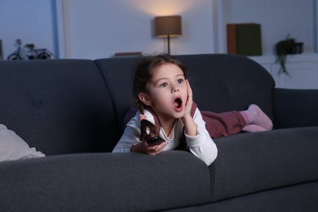 Shocked girl watching TV on sofa at homeの写真素材