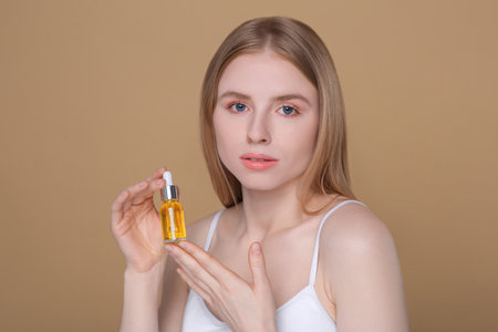 Beautiful young woman with bottle of essential oil on brown backgroundの写真素材