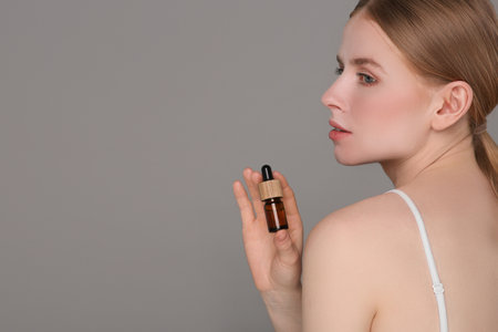Beautiful young woman with essential oil on light gray background. Space for textの写真素材