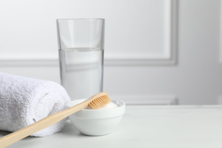 Bamboo toothbrush, bowl of baking soda, towel and glass of water on white table. Space for textの写真素材