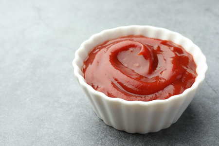 Bowl of tasty ketchup on light gray table, closeup. Space for textの写真素材