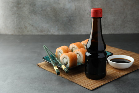 Tasty soy sauce, chopsticks and sushi rolls with salmon on gray table. Space for textの写真素材