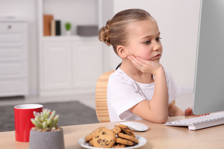 Little girl using computer at table in room. Internet addiction