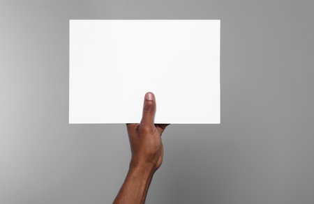 African American man holding sheet of paper on gray background, closeup. Mockup for designの写真素材