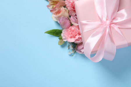 Gift box and beautiful flowers on light blue background, flat lay. Space for textの写真素材