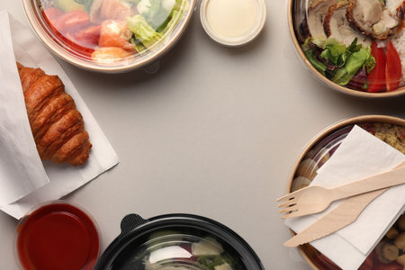 Tasty food in containers with wooden knife and fork on light gray table, flat lay. Space for textの写真素材