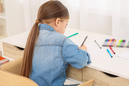 Cute little girl drawing with marker at desk in room. Home workplaceの写真素材