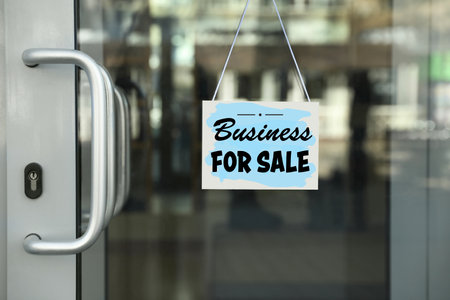 Light blue sign with Business For Sale hanging on glass doorの写真素材