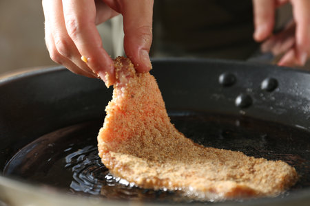 Cooking schnitzel. Woman putting raw pork chop in bread crumbs into frying pan, closeup