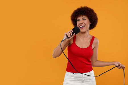 Curly young woman with microphone singing on yellow background, space for textの写真素材