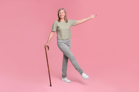 Senior woman with walking cane posing on pink backgroundの写真素材