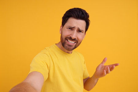 Emotional man taking selfie on yellow backgroundの写真素材