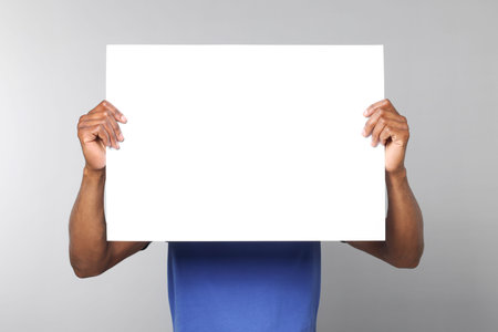 African American man holding sheet of paper on gray background. Mockup for designの写真素材