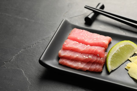 Tasty sashimi (pieces of fresh raw tuna) and lime wedge on black table, closeupの写真素材